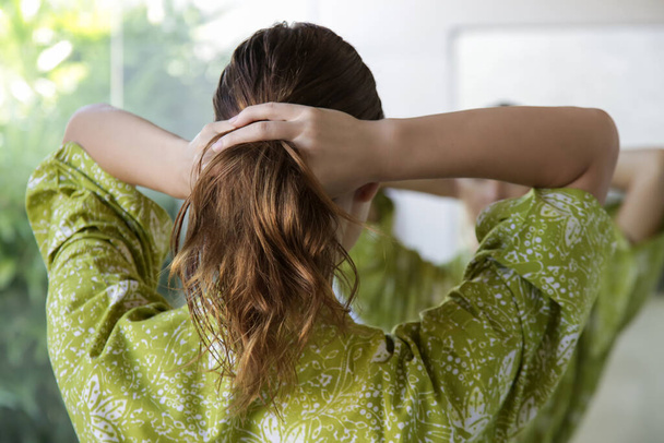 Jovem morena aplicando óleo de cabelo com os dedos no banheiro
 - Foto, Imagem
