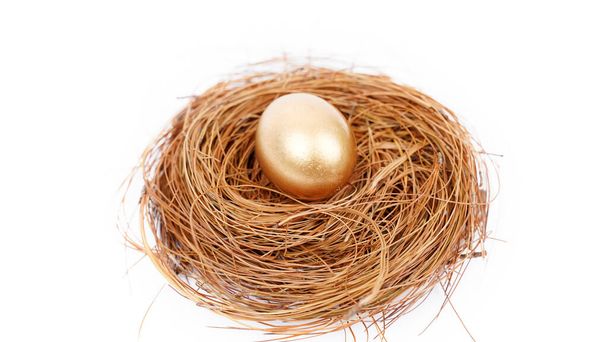 Nahaufnahme eines goldenen Eiers auf dem Stroh-Nest. Isoliert auf weißem Hintergrund - Foto, Bild