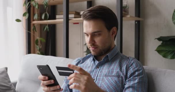 Happy man holding cellphone using credit card makes purchase - Кадри, відео