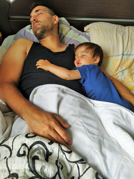 Πατέρας και γιος κοιμούνται κουρασμένοι στο κρεβάτι. - Φωτογραφία, εικόνα