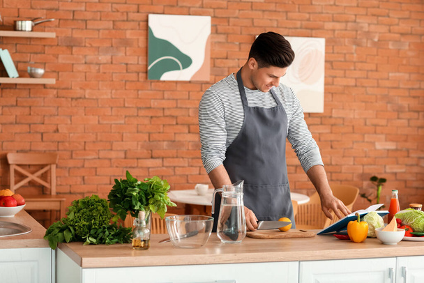 Молодой человек с книгой рецептов готовит свежий лимонад на кухне
 - Фото, изображение