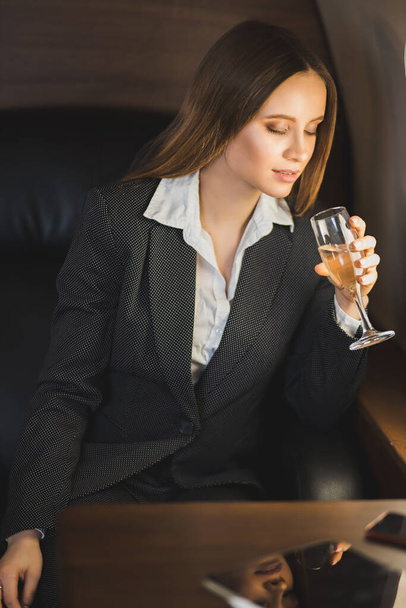 A beautiful confident caucasian business lady in suit, with makeup, long hair sitting in a private jet with a glass of champagne, celebrating success. Business concept. - Fotó, kép