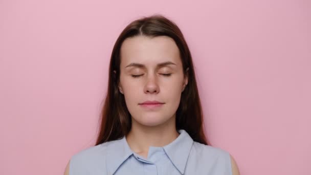Portrait of young positive woman with cheerful expression, dressed in blue shirt, cute happy brunette girl looking at camera, isolated over pink studio background. People sincere emotions concept - Felvétel, videó