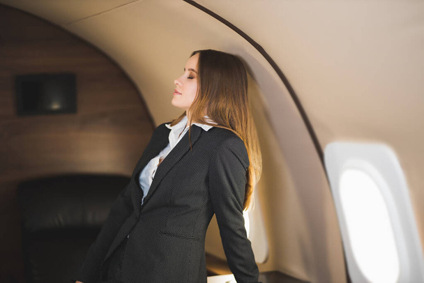 Traveling at first class. Flight with comfort. Beautiful successful caucasian young lady wearing stylish black suit in private aircraft. Business, success, travel concept. - Fotografie, Obrázek