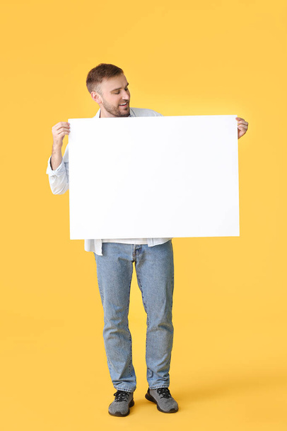 Young man with blank placard on color background - Фото, изображение