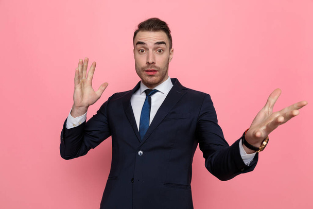 confused young businessman holding hands up and gesticulating, standing on pink background - Foto, Bild