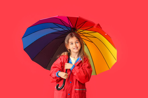 Cute little girl in raincoat and with umbrella on color background - Foto, Imagem