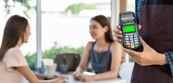 Panoramic closeup of waiter hand hold credit card reader for contactless payment with customers in restaurant background. New normal restaurant contactless payment concept. - Фото, зображення
