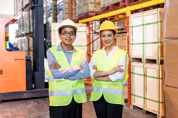Portrait of Asian warehouse manager and worker arm crossed with warehouse worker operate forklift to check inventory in background. Reopening business warehouse technology and logistic concept. - Foto, Imagem