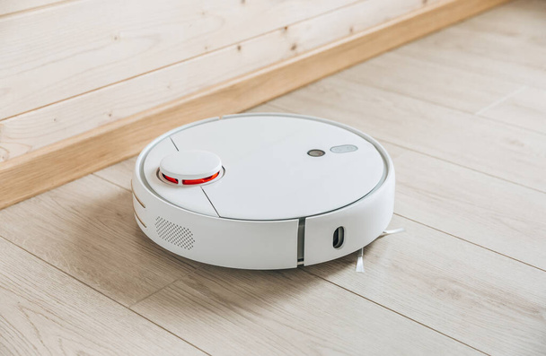Wireless robot vacuum cleaner working on wooden floor. Smart household technologies. - Foto, immagini