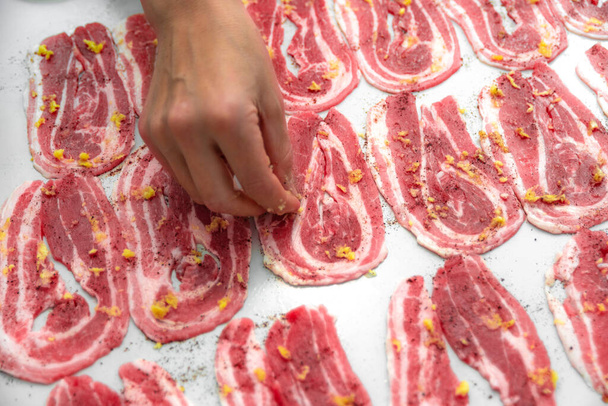 Mulher dona de casa picles fatias de bacon em fatias finas com alho e especiarias na mesa. Cozinhar lixo e alimentos gordurosos
 - Foto, Imagem
