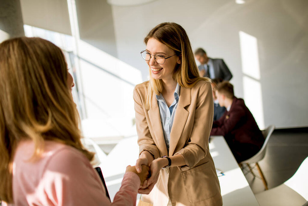 Two pretty young business women giving friendly handshake in the office - Photo, Image