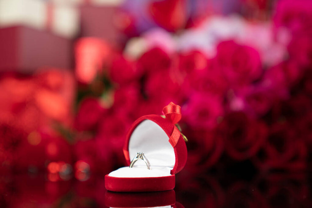 Concetto di giornata romantica. Anelli nuziali sdraiato sul tavolo splendente sullo sfondo rose rosse.  - Foto, immagini