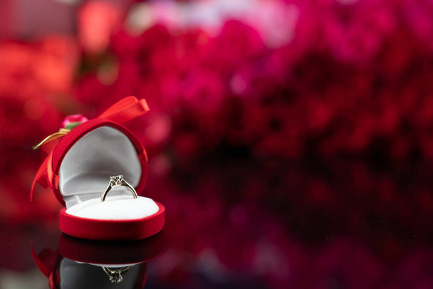 Romanttinen päivä konsepti. Vihkisormukset makaa paistaa pöydällä punaisia ruusuja taustalla.  - Valokuva, kuva
