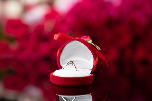 Romantic day concept. Wedding rings lying on shining table on the red roses background.  - Photo, Image