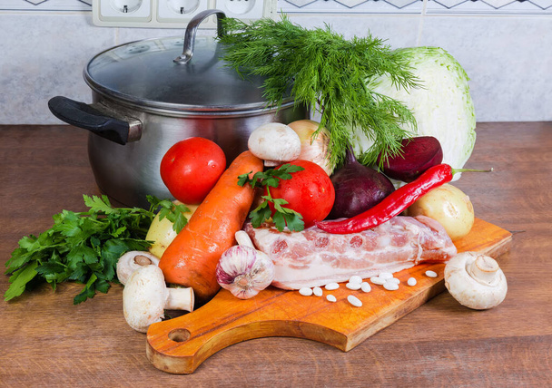 Typowe surowce do gotowania typowego czerwonego buraczanego barszczu - żeberka wieprzowe, świeże warzywa, fasola i zioła na desce do krojenia, pusty garnek na stole kuchennym - Zdjęcie, obraz