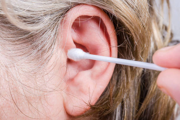 Tampone di cotone tenere per le dita vicino all'orecchio umano prima della pulizia del condotto uditivo, primo piano a fuoco selettivo - Foto, immagini