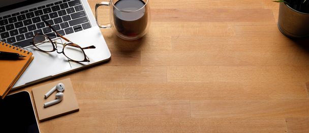 Tiro cortado de mesa de trabalho na moda com espaço de cópia, laptop, xícara de café e suprimentos na mesa de madeira
  - Foto, Imagem