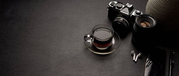 ブラックレザーテーブルの上にコーヒーカップ、カメラ、電源、装飾やコピースペースとモダンなオフィスデスクの作物のショット  - 写真・画像
