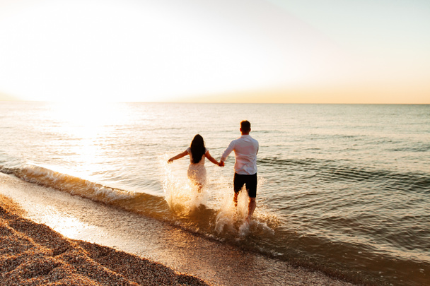Loving couple in white clothes during a honeymoon at sea walk on the sand at a photoshoot Love Story, ocean coast, beach - Photo, Image