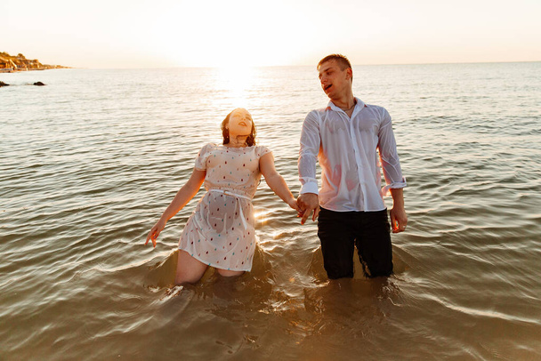 Couple amoureux en vêtements blancs lors d'une lune de miel en mer marcher sur le sable lors d'une séance photo Love Story, côte océan, plage - Photo, image