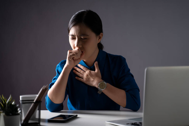 Mulher asiática de camisa azul estava doente de febre, trabalhando em um laptop no escritório. isolado em fundo branco. Tecla baixa
. - Foto, Imagem