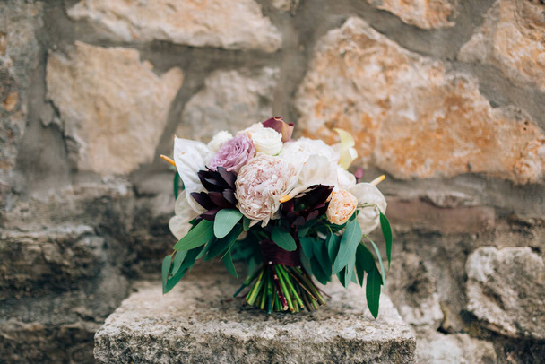 свадебный букет белых и розовых пионов, роз, ветвей эвкалипта, каллы и декоративной артишоки на камне
 - Фото, изображение