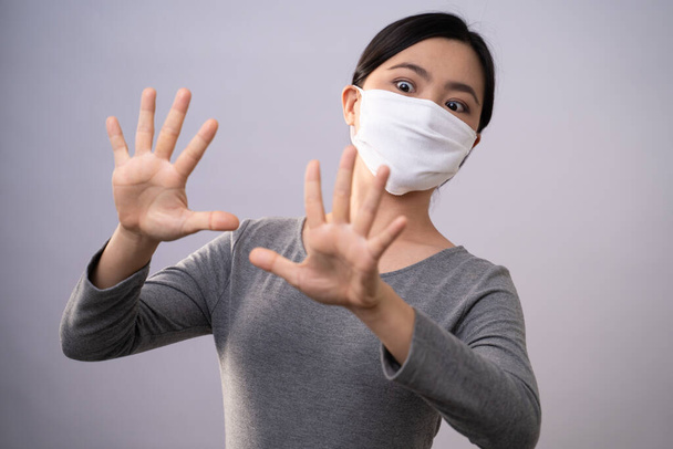 Не прикасайся к лицу. Азиатка в защитной маске, показывающая, что рука делает знак "стоп" стоящим изолированным на заднем плане. Профилактика коронавируса COVID-19
. - Фото, изображение