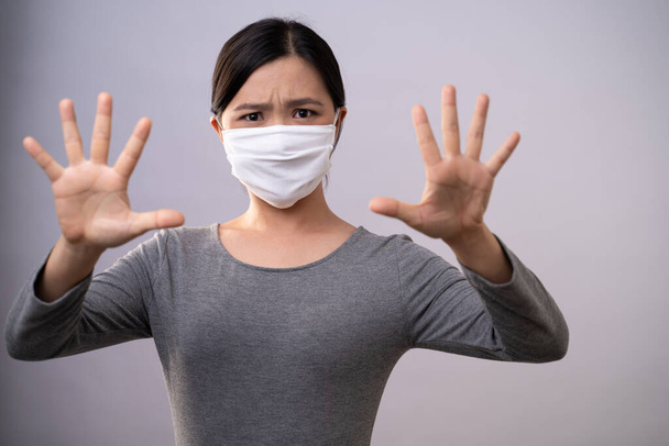 顔に手を出すな。背景に独立した立ち位置にストップサインを作る手を示す保護顔のマスクを身に着けているアジアの女性。予防コロナウイルスCOVID-19の概念. - 写真・画像
