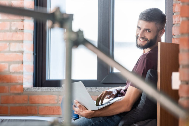 επιλεκτική εστίαση του χαρούμενου επιχειρηματία που κάθεται στον πάγκο παράθυρο και τη χρήση φορητού υπολογιστή  - Φωτογραφία, εικόνα