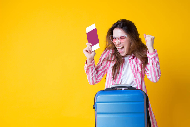 Joyeux heureux belle jeune femme brune avec passeport, billet, valise, faire geste gagnant isolé sur fond jaune.Fille touristique en vêtements d'été, lunettes de soleil profiter voyage à l'étranger - Photo, image
