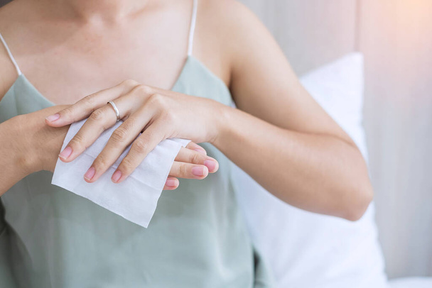 Kobieta czyszcząca ręce mokrymi chusteczkami i środkiem dezynfekującym alkohol na łóżku podczas budzenia w domu, zakażenie ochronnym koronawirusem (Covid-19). Styl życia, nowa, normalna i czysta koncepcja powierzchni - Zdjęcie, obraz