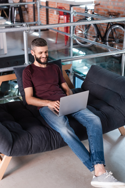 usměvavý podnikatel sedí na pohovce a používá notebook v kanceláři - Fotografie, Obrázek