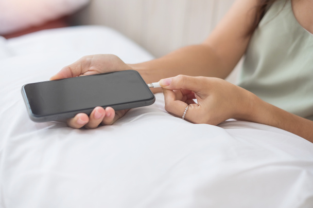 Femme mains charge la batterie dans le téléphone intelligent mobile dans la chambre à coucher à la maison. Technologie, partage multiple et concepts de style de vie - Photo, image