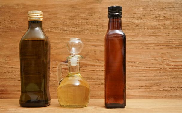 Backdrop of three different olive oil glass transparent bottles with cork stand on wooden board. kitchen space room.  Empty space for inscription  - Valokuva, kuva
