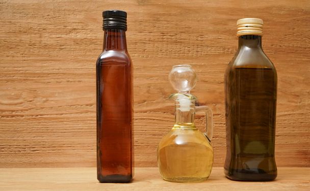 Backdrop of three different olive oil glass transparent bottles with cork stand on wooden board. kitchen space room.  Empty space for inscription  - Foto, afbeelding