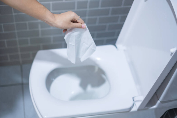 Woman hand throw paper towels in the toilet bowl. Cleaning, Lifestyle and personal hygiene concept - Zdjęcie, obraz