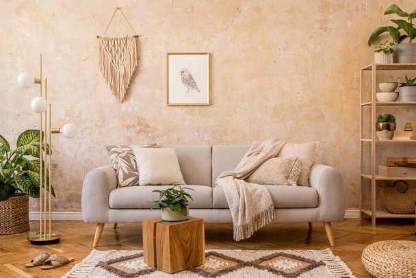 Stylish scandi compostion at living room interior with design gray sofa, wooden coffee table, shelf, cube, carpet, rattan pouf, plants, picture frame, table lamp and elegant accessories in home decor. - 写真・画像