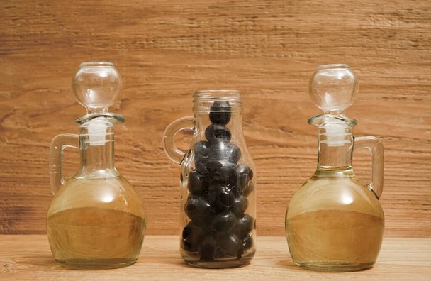 2 two jars with olive oil and some black olives isolated on wooden board background.                                                         - Foto, immagini