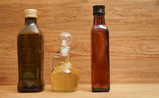 Backdrop of three different olive oil glass transparent bottles with cork stand on wooden board. kitchen space room.  Empty space for inscription  - Foto, Imagem