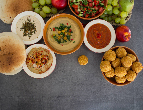 中東の本格的な料理。フムス、ファラフェル、ピタパン、ハリッサソース、タヒニ、新鮮なサラダと果物のプレート。イスラエルの伝統的な食事のトップビューの写真。カラフルな食べ物の絵. - 写真・画像