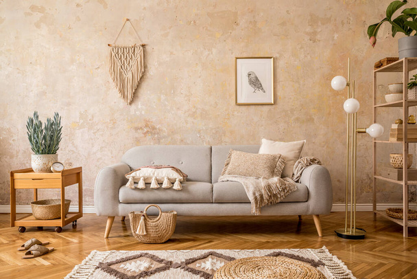 Stylish scandi compostion at living room interior with design gray sofa, wooden coffee table, shelf, cube, carpet, rattan pouf, plants, picture frame, table lamp and elegant accessories in home decor. - Foto, Imagem