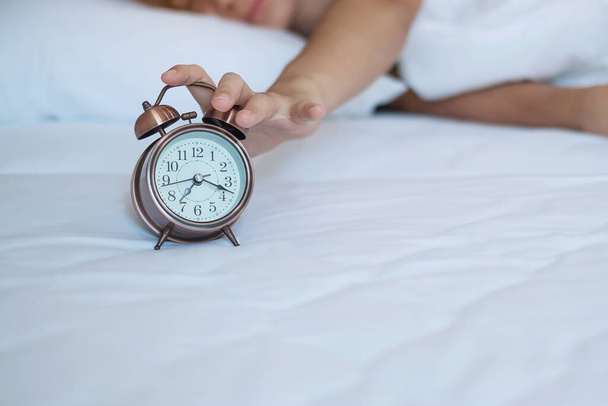 alarm clock and asian woman hand stop time in bed while sleeping, young adult female wake up late in the morning. fresh relax, sleepy and have a nice day concepts - Photo, Image