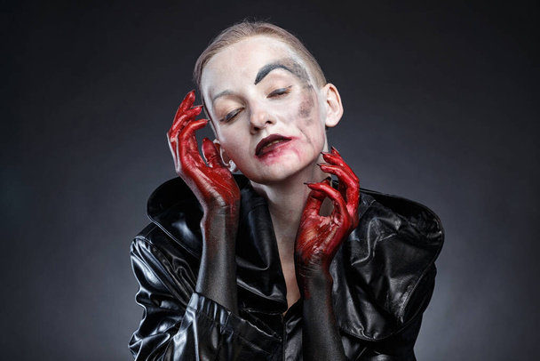 Portré horror nő fekete esőkabátban piros kezekkel az arc közelében - Fotó, kép