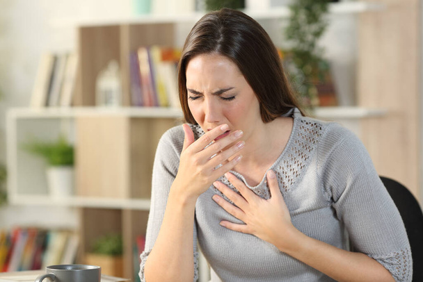 Sick woman coughing or wheezing sitting on a desk in the living room at home - Фото, изображение