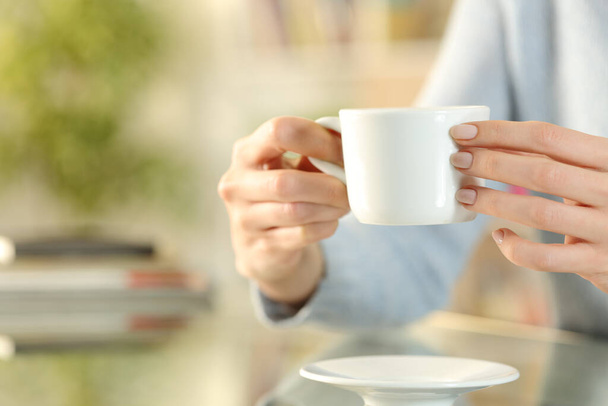 Close up of woman hands holding coffee cup sitting on a desk in the living room at home - Foto, Imagem