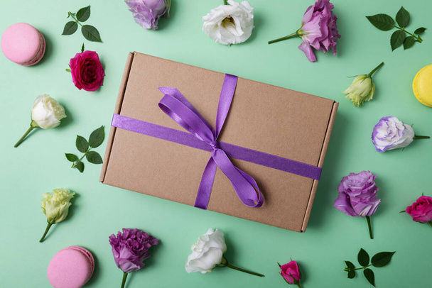 gift box with purple ribbon and flowers on green background. top view - Фото, изображение