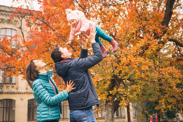 Casual family couple with daughter on a free time in park. Autumn cloudy weather with fallen leafs. Copy space - Photo, Image