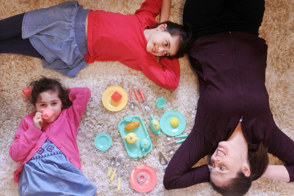 Luchtfoto van een moeder en dochters die samen spelen tijdens een theekransje in een speelkamer terwijl ze naar elkaar kijken. Echte mensen. Kopieerruimte - Foto, afbeelding