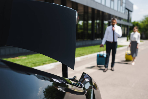 Selective focus of business people with suitcases walking to car on urban street  - Фото, зображення